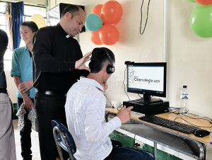 El Pbro. Eduin Salazar rector del cibercolegio ayudando a un estudiante en el nuevo centro aprende.