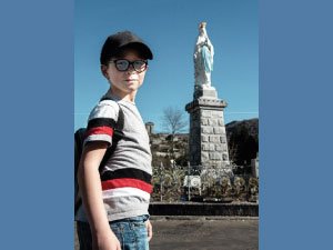 Imagen de un niño visitando la virgen de Lourdes