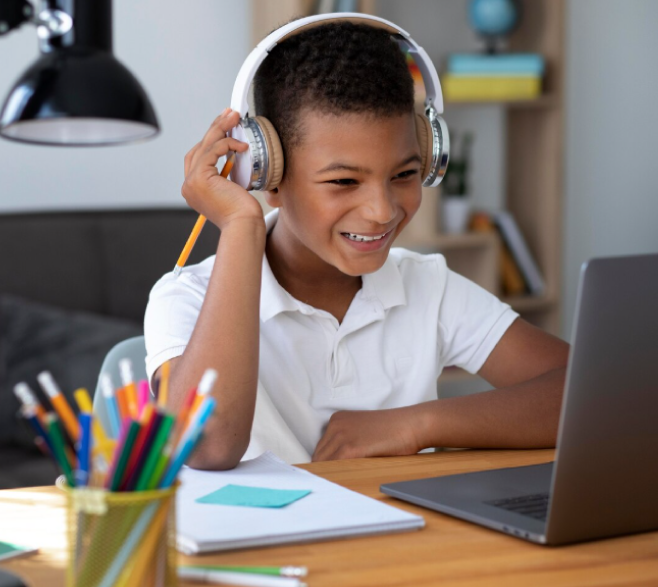 Niño con uniforme escolar blanco y unas diademas sentado al frente de un computador portátil.